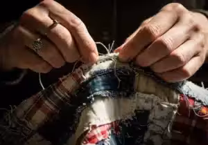 Hands stitching rags, symbolizing resourcefulness and humble beginnings.